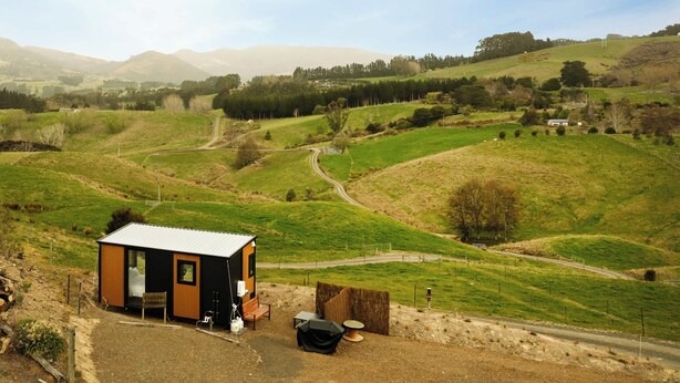 Eine kleine, moderne Holzhütte mit einem Zimmer, einer Veranda und einem Essbereich.