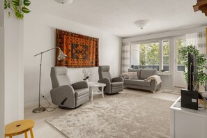 A living room with two grey armchairs, a white coffee table, a grey sofa, and a large window with blinds.