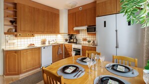 A modern kitchen with wooden cabinets, a dining table set for four, and a refrigerator. - Comfy City Centre Apartment in Rovaniemi (Rovaniemi)