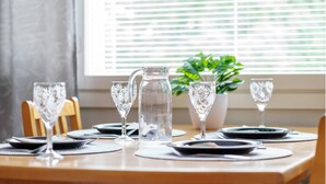 A dining table set with plates, cutlery, and clear glassware, with a pitcher and a potted plant in the background. - Comfy City Centre Apartment in Rovaniemi (Rovaniemi)