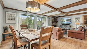 A spacious living area with a wooden dining table, leather sofas, and a stone fireplace. - Breck Condo | Private Balcony & Trail Access (Breckenridge)