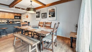 A dining area with a wooden table, chairs, and a bench. There are framed pictures on the wall and a hanging light fixture above the table. - Breck Condo | Private Balcony & Trail Access (Breckenridge)