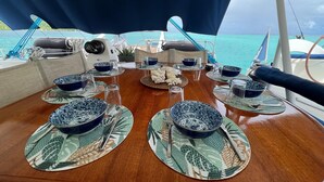 Une table à manger dressée avec de l’assiette, des bols et des couverts aux motifs bleus et blancs, avec une vue sur la mer et des bateaux en arrière-plan.