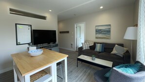 A modern living room with a flat-screen TV, a wooden coffee table, a grey sofa, and a small armchair.