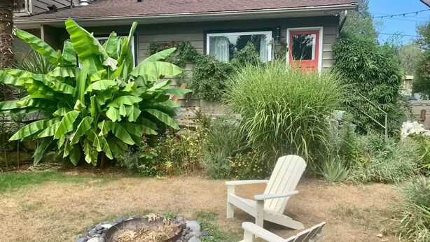 A house with a fire pit and two Adirondack chairs in the yard.
