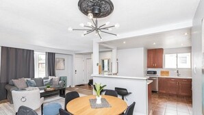 A modern living room with a round wooden table, black chairs, and a ceiling fan.