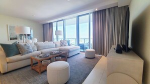 A modern hotel room with a large sofa, a coffee table, and a TV on a stand.