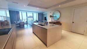 A modern kitchen with a central island, a dining area with a sofa and chairs, and a large window offering a view.