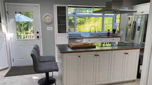 A modern kitchen with white cabinetry, a central island, a built-in oven, and a window overlooking greenery.