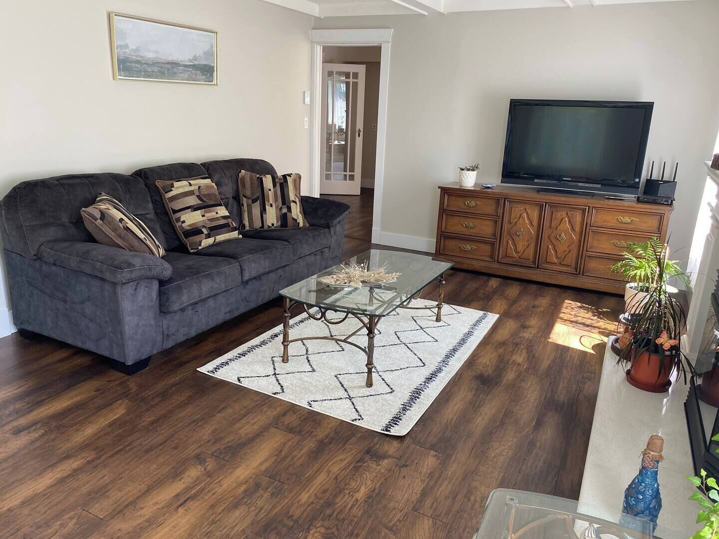 Ein Wohnzimmer mit einem dunkelgrauen Sofa, einem Glastisch und einem Holzschrank mit Fernseher.
