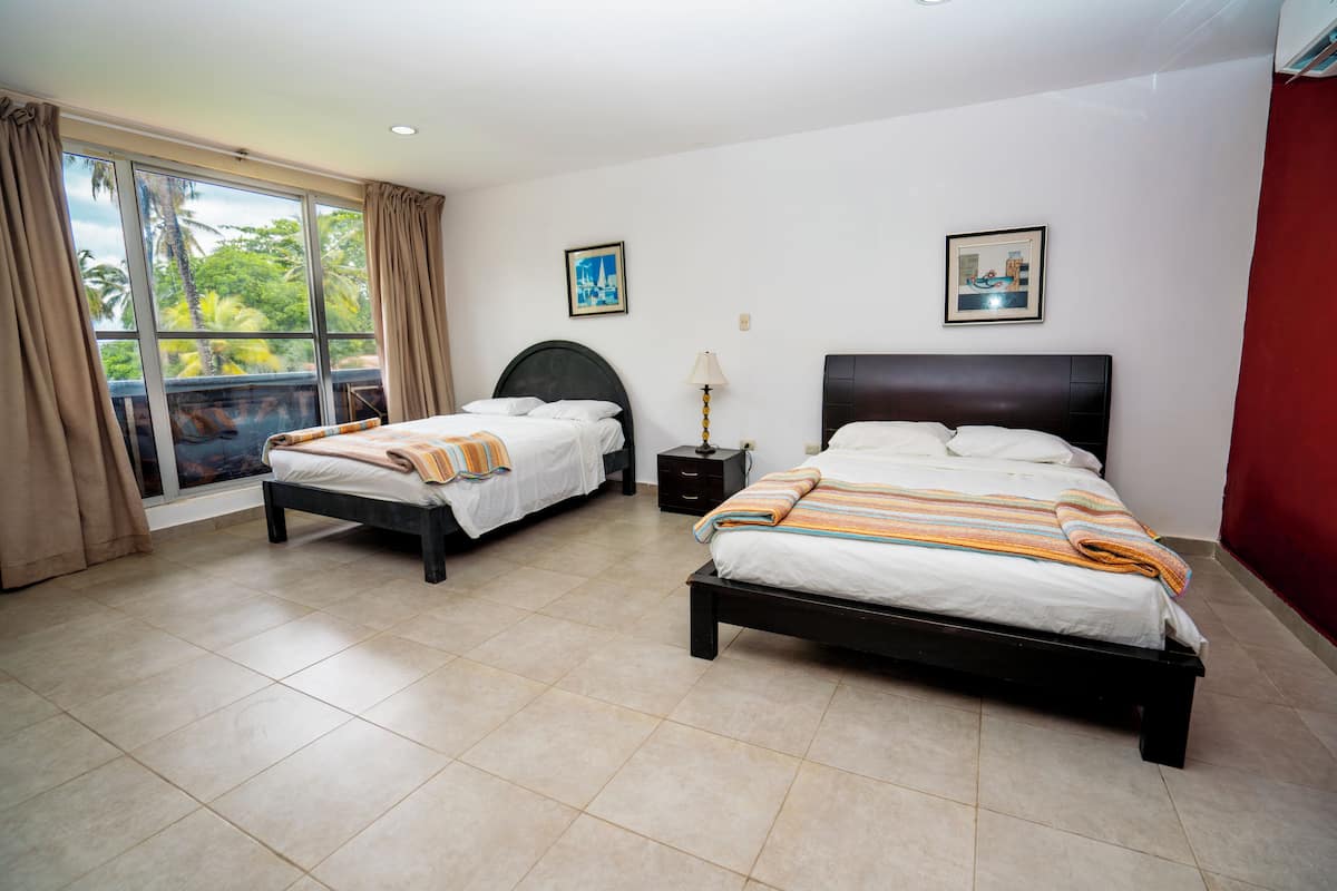 A hotel room with two beds, a large window with curtains, and artwork on the walls.