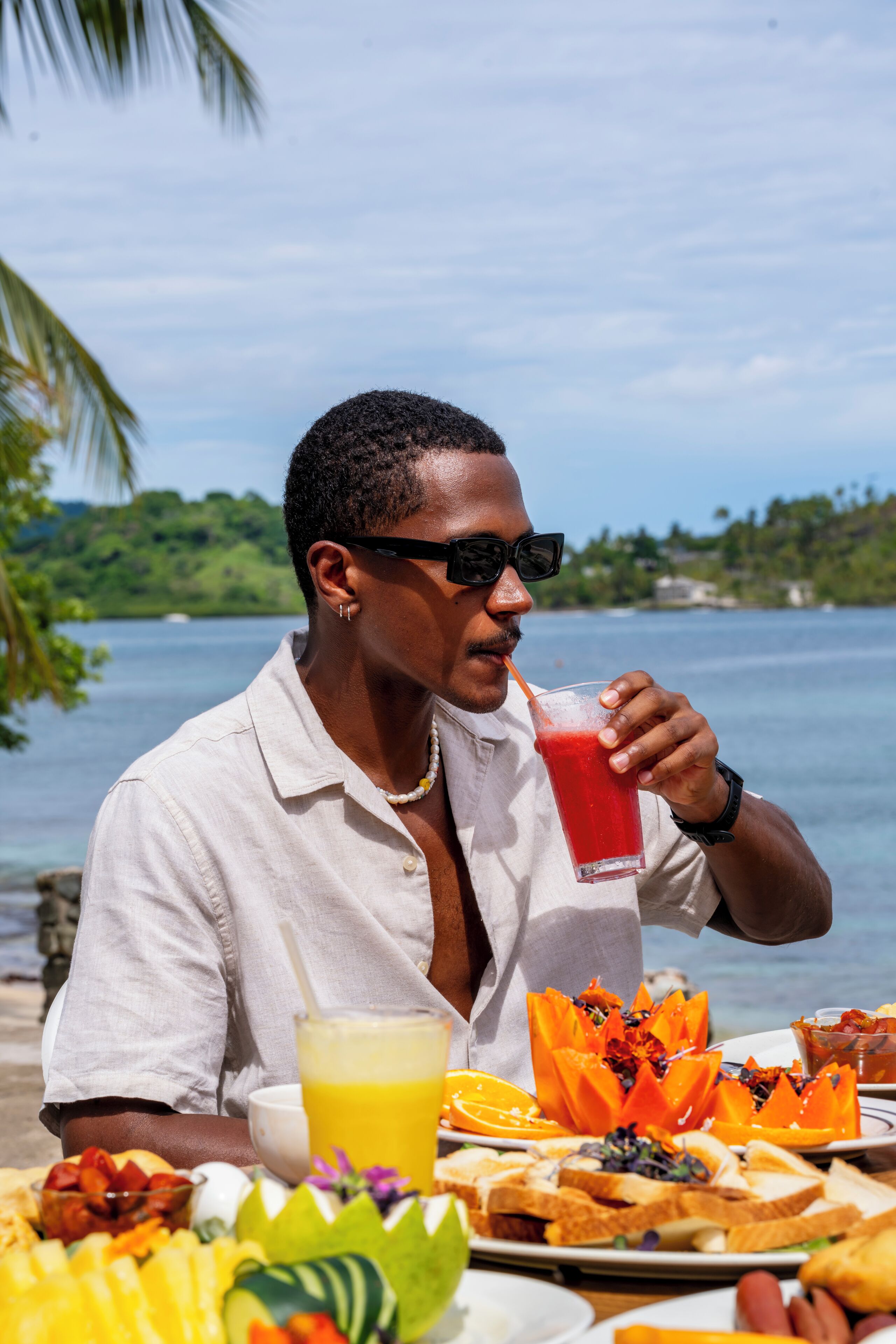 A person sitting at a table with a meal and a drink, overlooking a body of water.