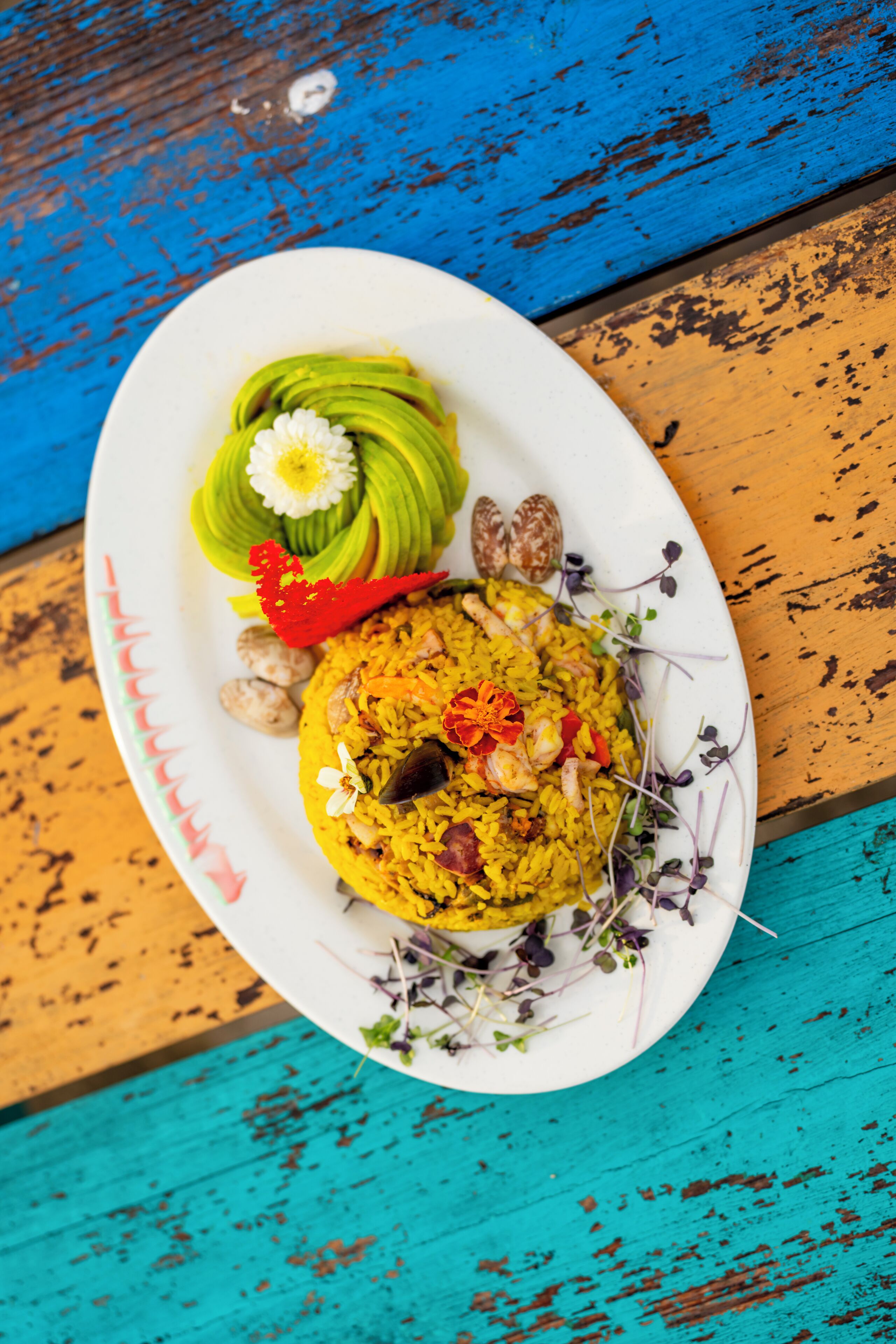 A plate of food with yellow rice, avocado slices, and garnishes on a white plate.