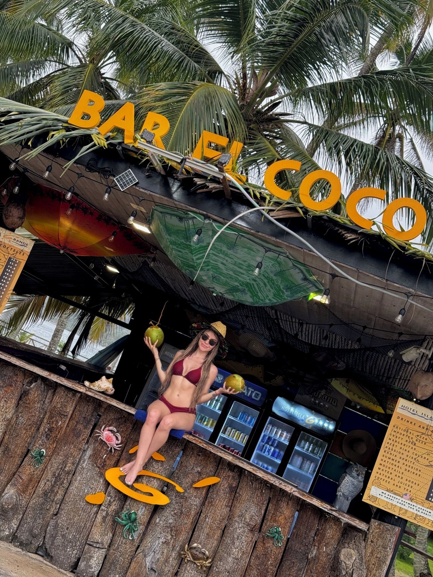Un bar de playa llamado "BAR EL COCO" con temática tropical, que incluye palmeras y una estructura de madera.