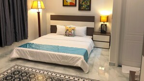 Habitación de hotel con cama, dos lámparas de noche, una mesita de noche, un ventanal con cortinas y dos cuadros colgados en la pared.