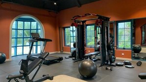 Un gimnasio con equipo de ejercicio, una pelota grande para hacer ejercicio y ventanales con vista a zonas verdes.