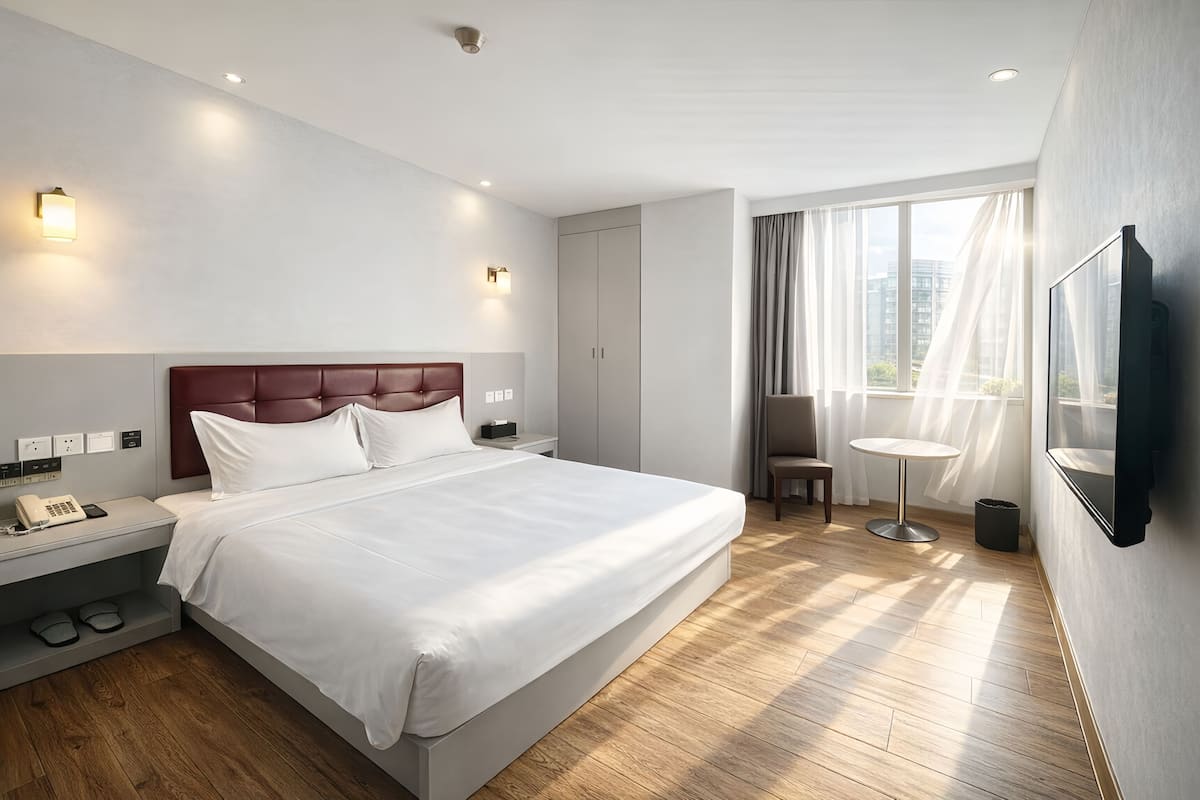 Una habitación de hotel moderna con una cama grande, mesita de noche, lámpara y una pequeña mesa redonda.