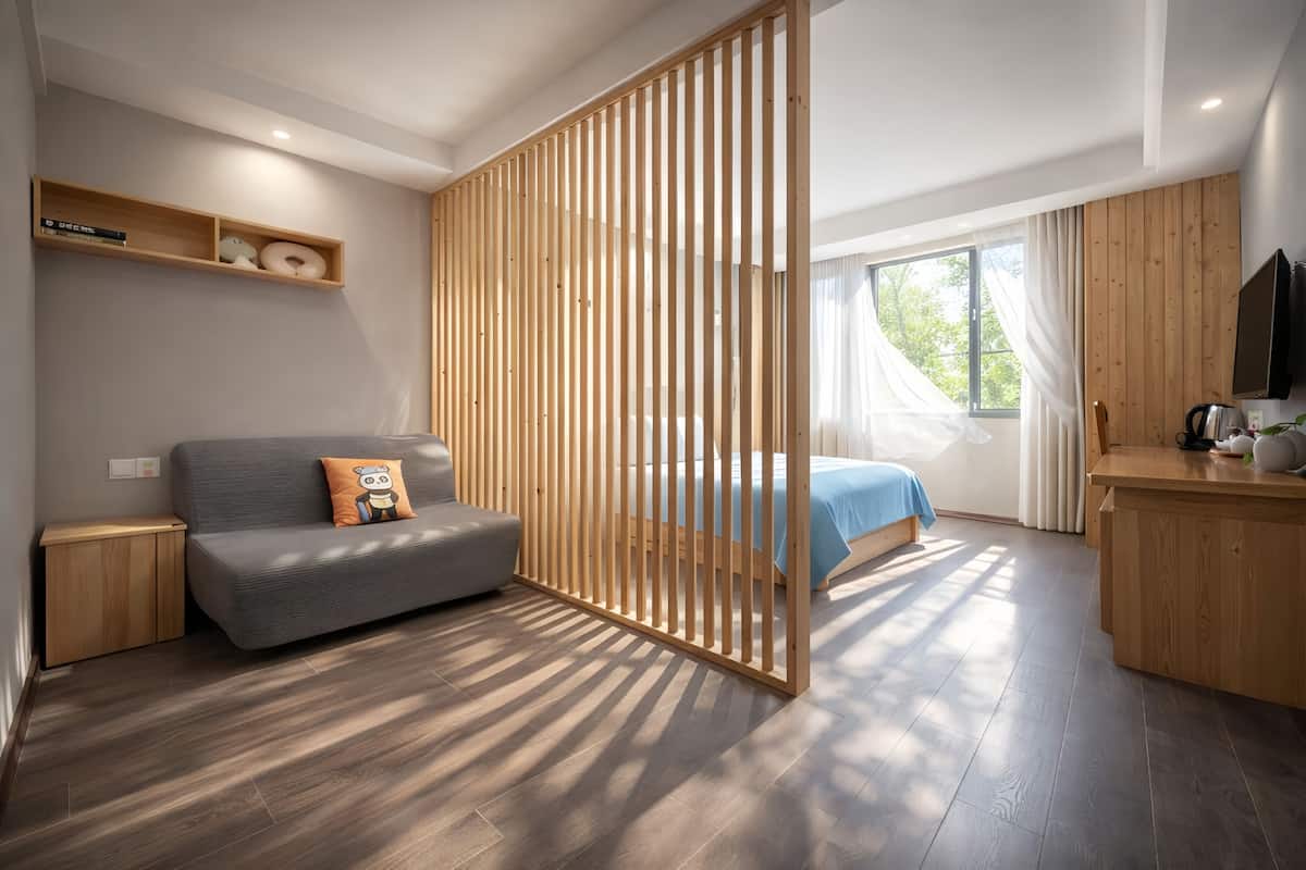 Un dormitorio moderno con un separador de madera, un sofá, una cama, un televisor y un escritorio de madera.