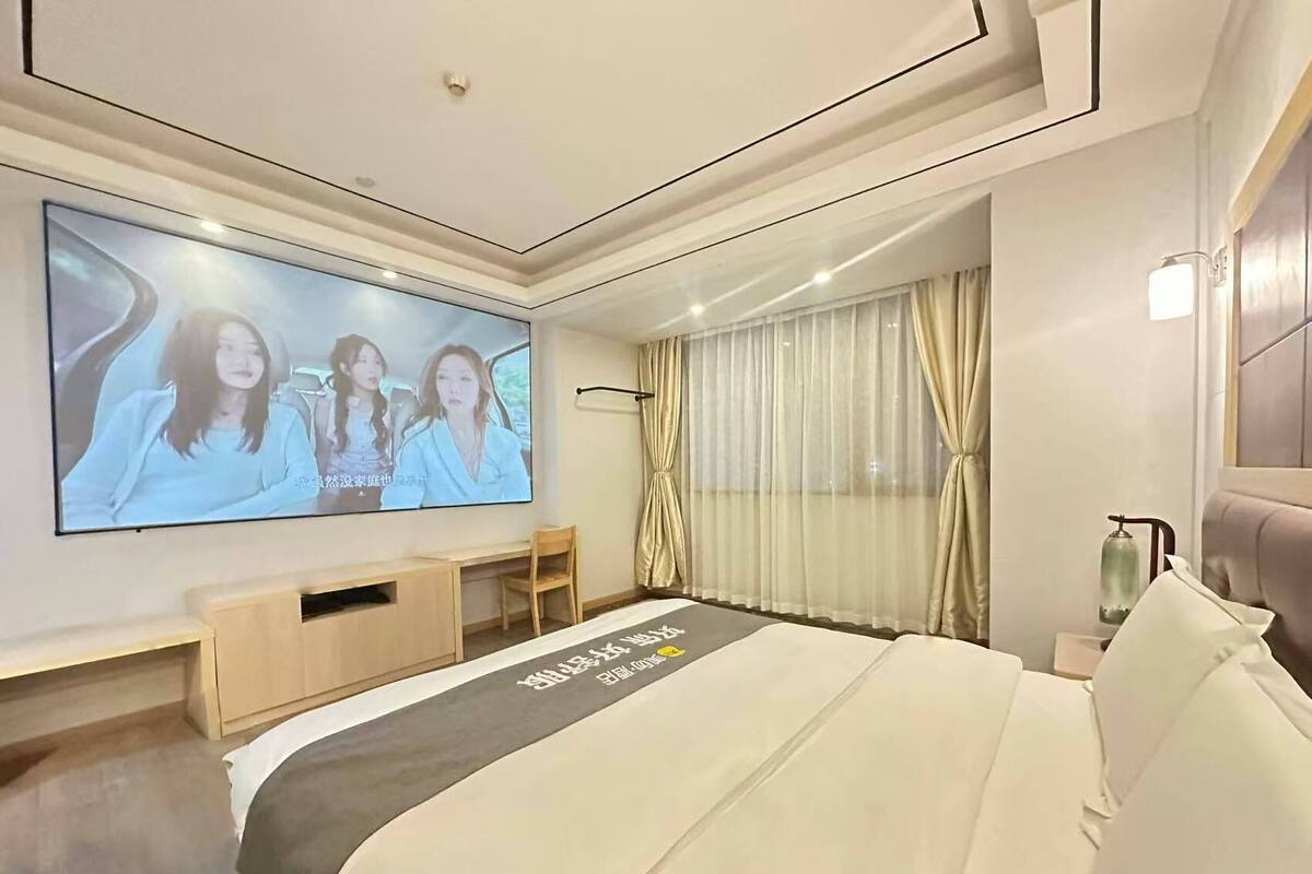 Una habitación de hotel con una cama grande, un televisor en la pared, un escritorio y una ventana con cortinas.