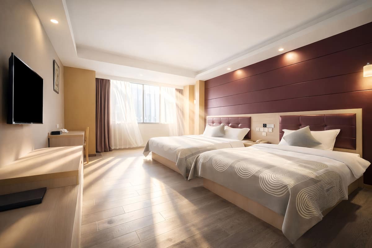 Habitación de hotel con dos camas, televisión, mesita de noche y un gran ventanal con cortinas.