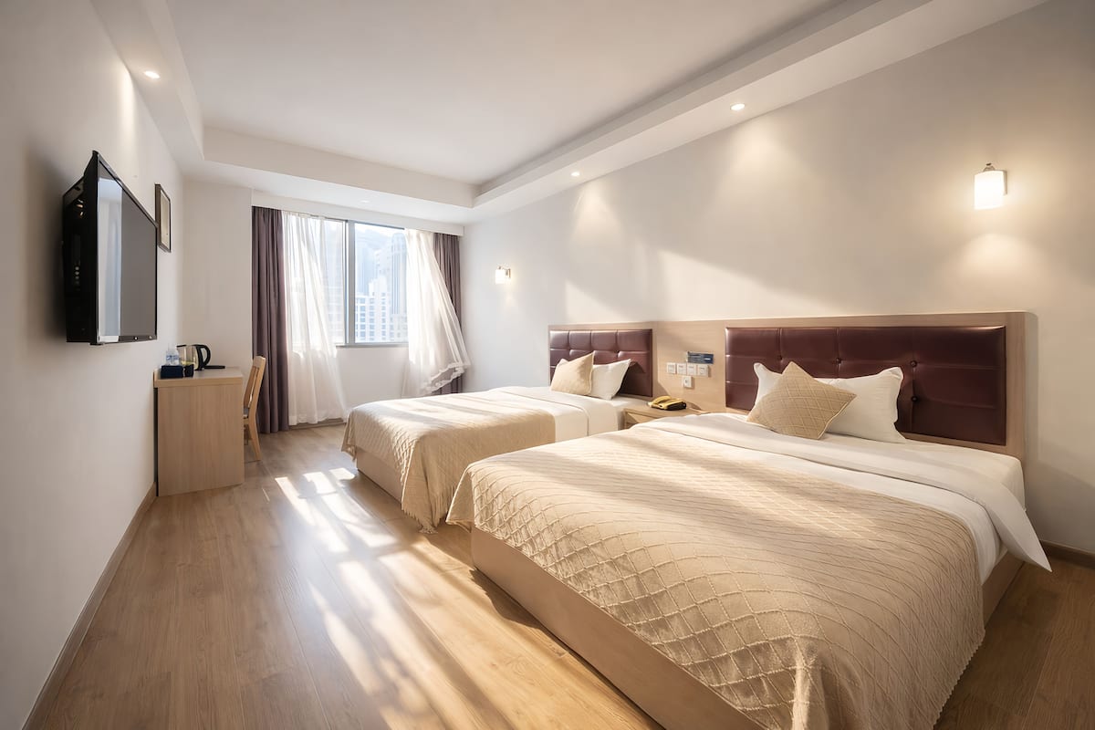 Habitación de hotel con dos camas, una televisión de pantalla plana, una mesita de noche, una ventana con cortinas y vistas a la ciudad.