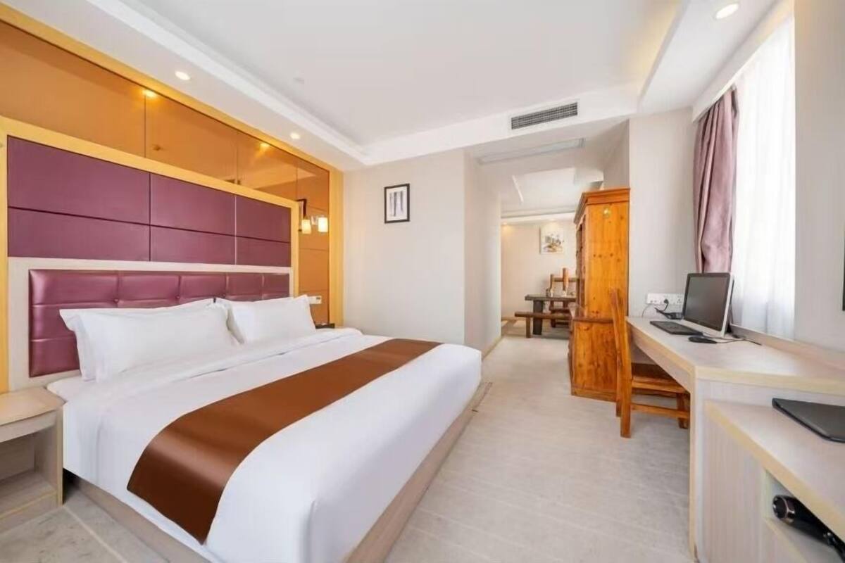 Una habitación de hotel con una cama grande, un escritorio con computadora y un armario de madera.