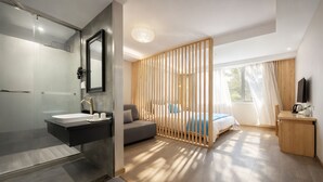 Een moderne hotelkamer met een glazen douchecabine, een houten scheidingswand, een bed met blauw beddengoed en een houten bureau.