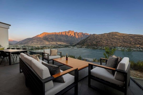 Una terraza con mobiliario exterior, vistas a montañas y una masa de agua.