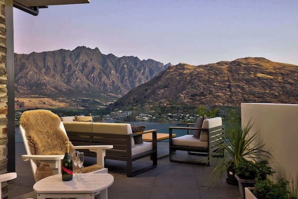 Une terrasse avec des meubles d’extérieur, une bouteille de champagne et une vue sur les montagnes.