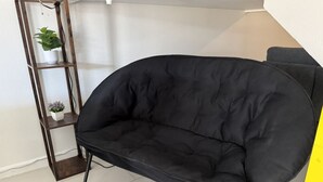 Una poltrona nera imbottita con gambe in metallo, uno scaffale di legno con piante e una parete gialla.