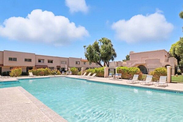 A swimming pool with lounge chairs and a building with a flat roof in the background.