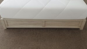 Una cama bien hecha con edredón blanco, dos almohadas y una toalla enrollada. Hay dos mesitas de noche con lámparas y tres obras de arte colgadas en la pared sobre la cama.
