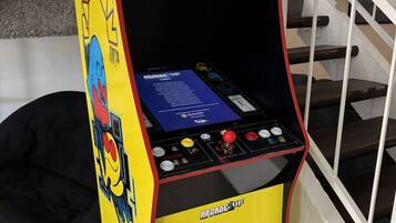 Una máquina de videojuegos arcade de Pac-Man con una combinación de colores amarillo y rojo, situada en una habitación con una escalera.