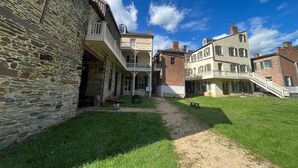 A courtyard with a stone building, a brick building with a balcony, and a grassy area. - Mountain Bungalow | Nature, History| Wineries|PS5 (Harpers Ferry)