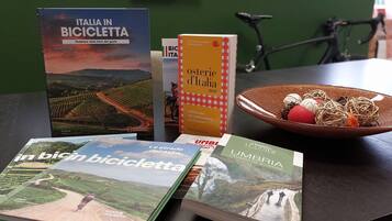 Une table avec plusieurs guides de voyage, un bol de nourriture et un vélo à l’arrière-plan.