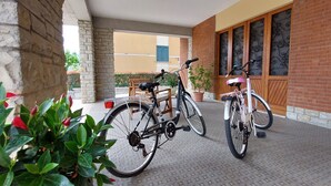 Un espace extérieur abrité où sont garés deux vélos, à proximité d’un bâtiment aux murs en briques et en pierres, agrémenté de plantes en pot et doté d’un sol carrelé.