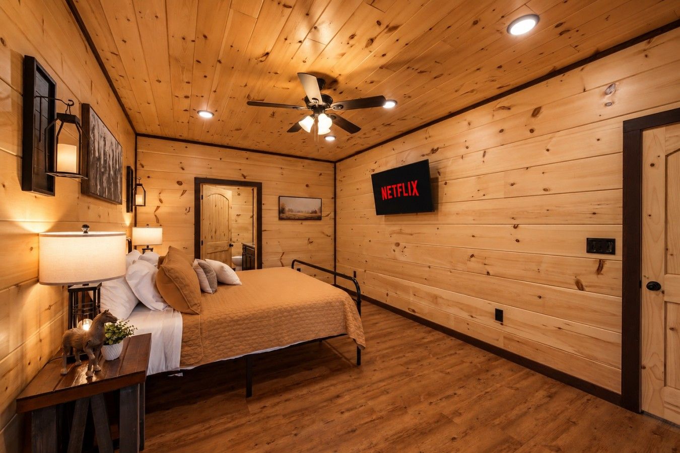 A wooden-paneled room with a bed, bedside lamps, a ceiling fan, and a wall-mounted Netflix sign.