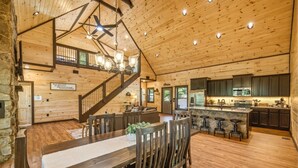 A spacious wooden interior with a dining area, kitchen, and a staircase leading to an upper level. - Dollywood 28 min | Game Room + Hot Tub + Fire Pit (Sevier County)