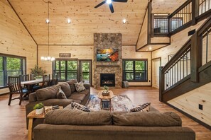 Amplia sala de estar con chimenea de piedra, techo de madera y ventanas grandes.