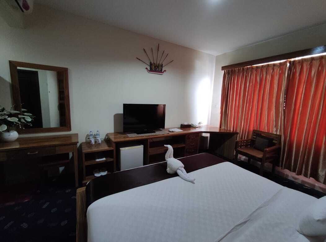 Habitación de hotel con cama, escritorio con televisor, una silla, espejo y ventana con cortinas.