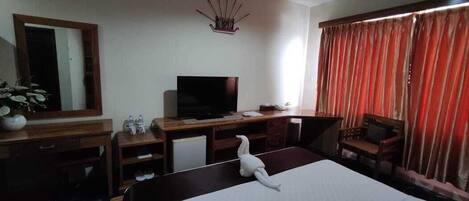 Habitación de hotel con cama, escritorio con televisor, una silla, espejo y ventana con cortinas.