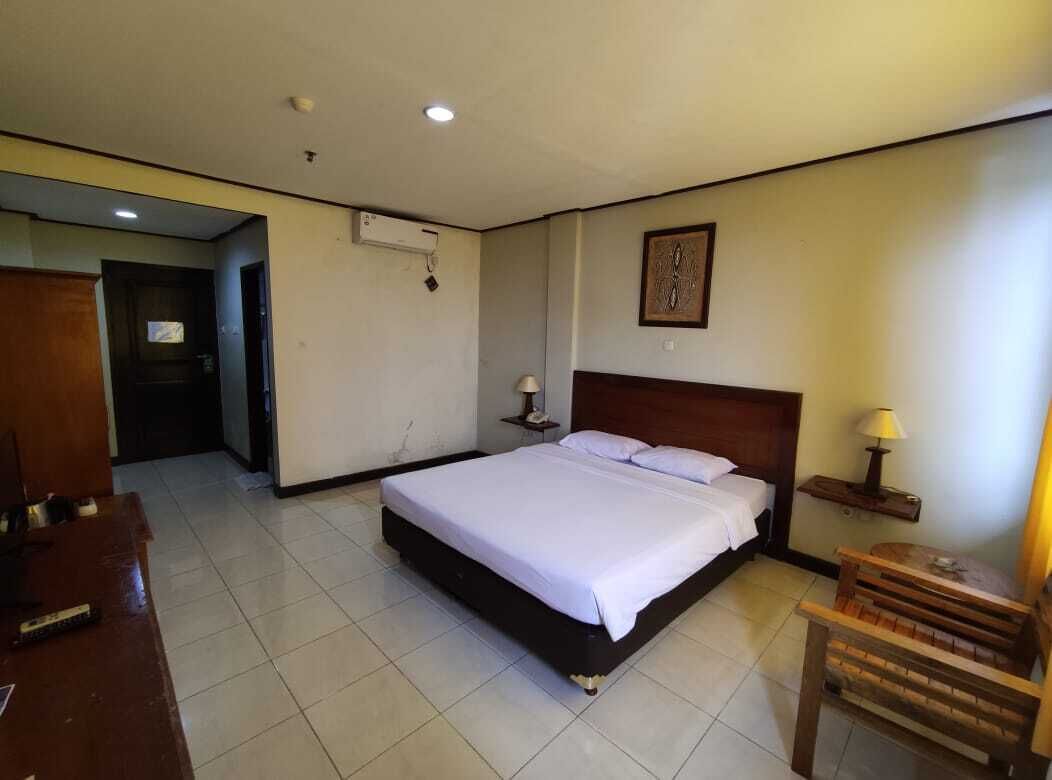Habitación de hotel con una cama grande, un escritorio, una silla, una mesita de noche con lámpara y aire acondicionado instalado en la pared.
