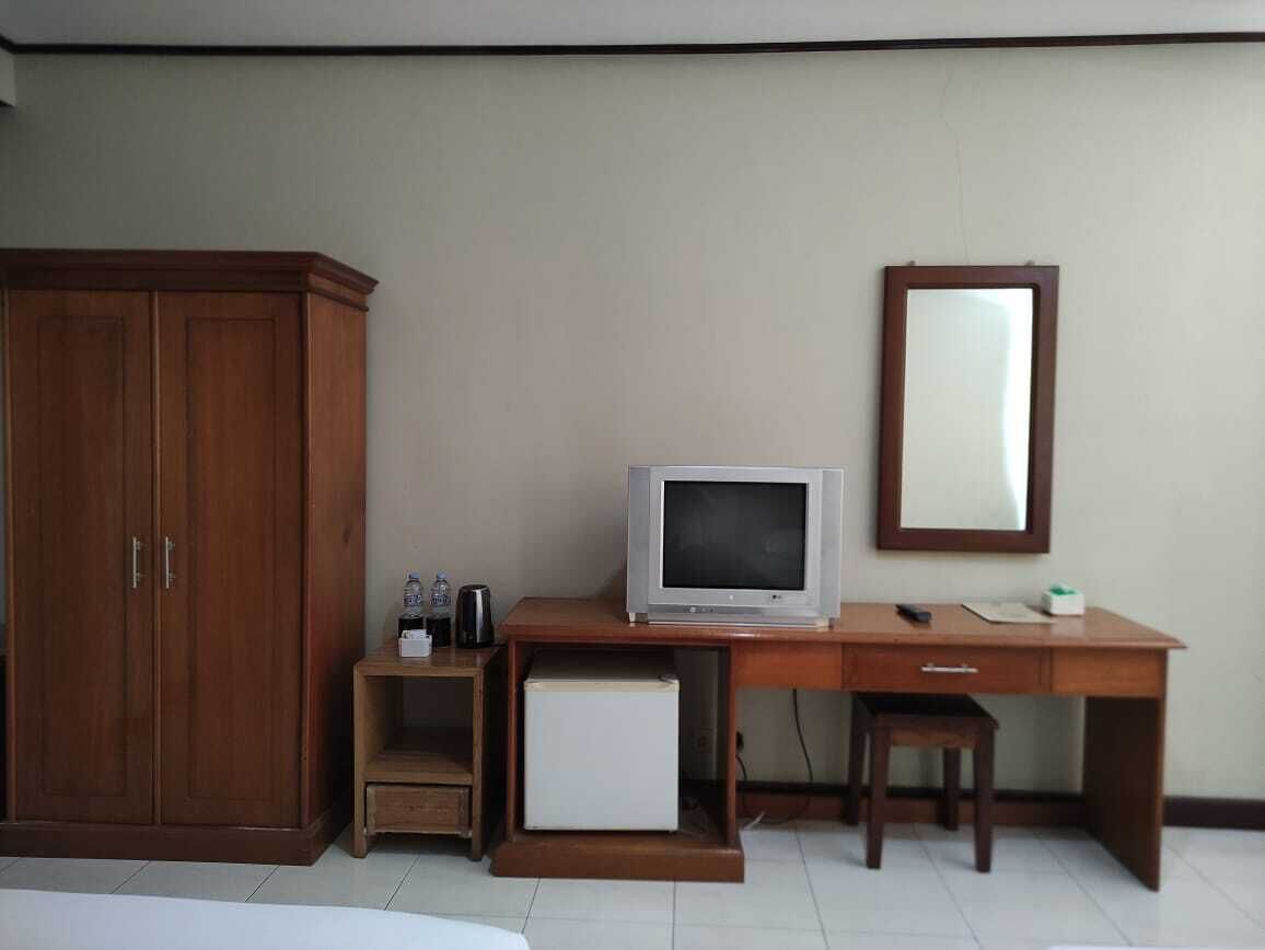 Une chambre avec une armoire en bois, un bureau avec une télévision, un petit réfrigérateur et un miroir.