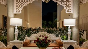 Una habitación tradicional con un sofá ornamentado en el centro, dos mesitas de noche con lámparas y un espejo decorativo sobre el sofá.