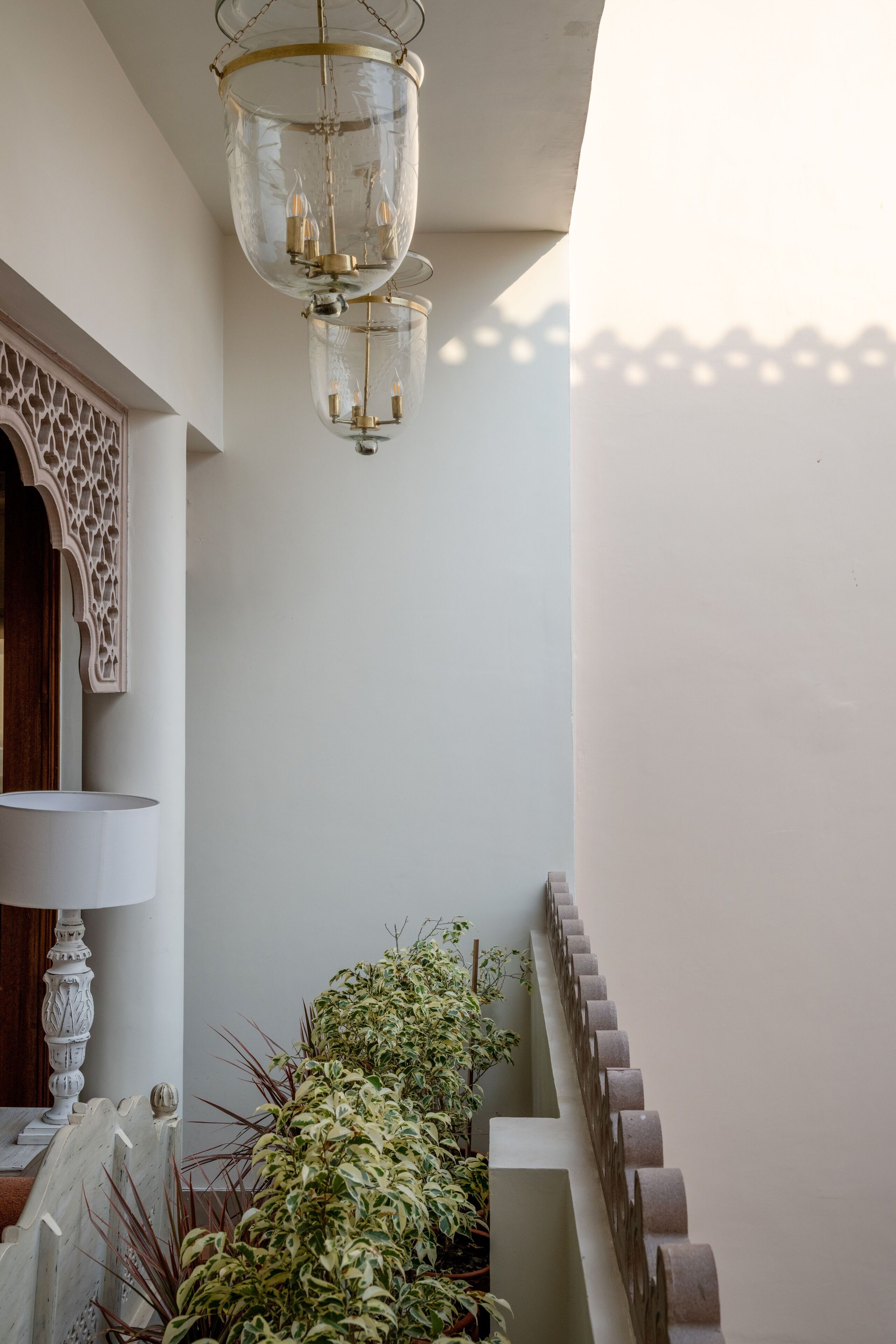 A staircase with a white railing, a clear glass chandelier, and a white wall with a decorative wooden panel.