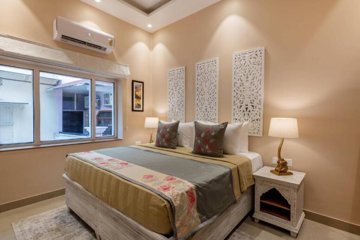 A bedroom with a bed, two bedside lamps, a window, and decorative panels on the wall.