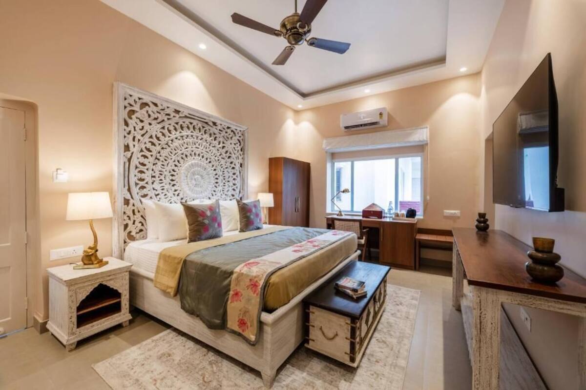 A bedroom with a bed, bedside tables, a desk, a chair, a ceiling fan, and a television.