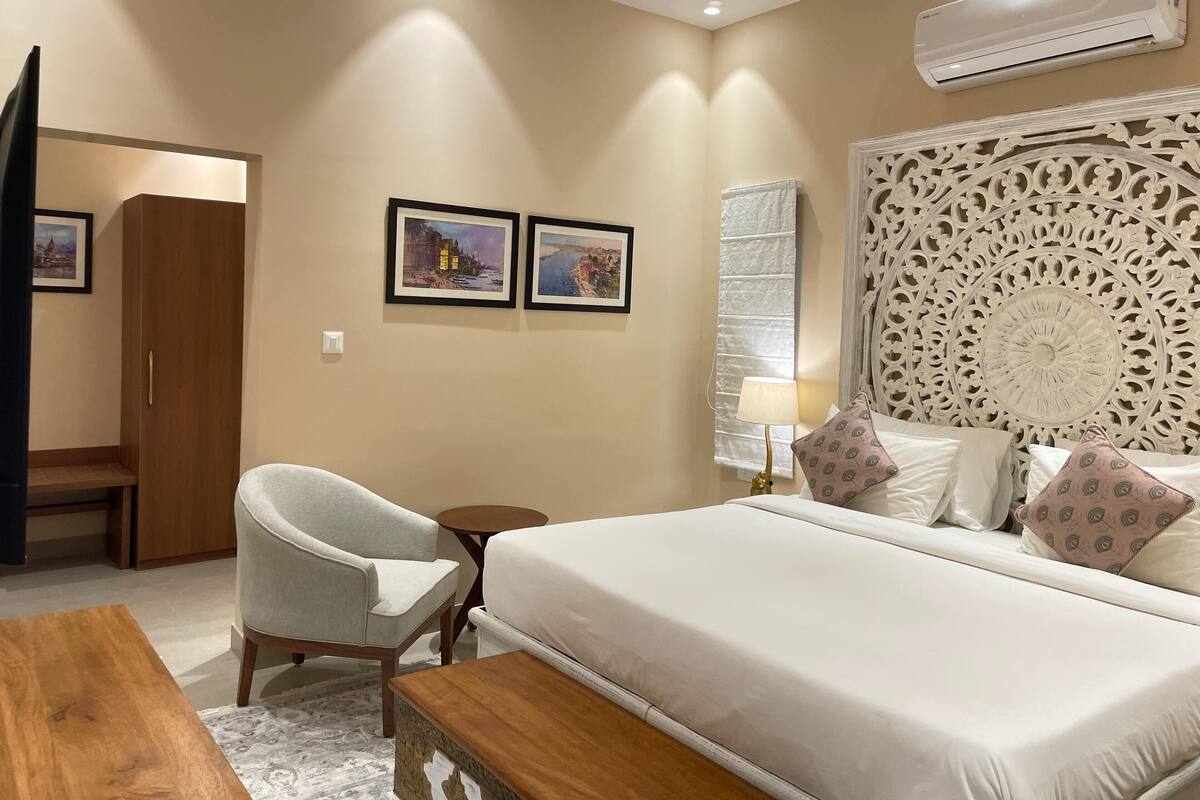 A hotel room with a bed, a chair, a small table, and an air conditioning unit.