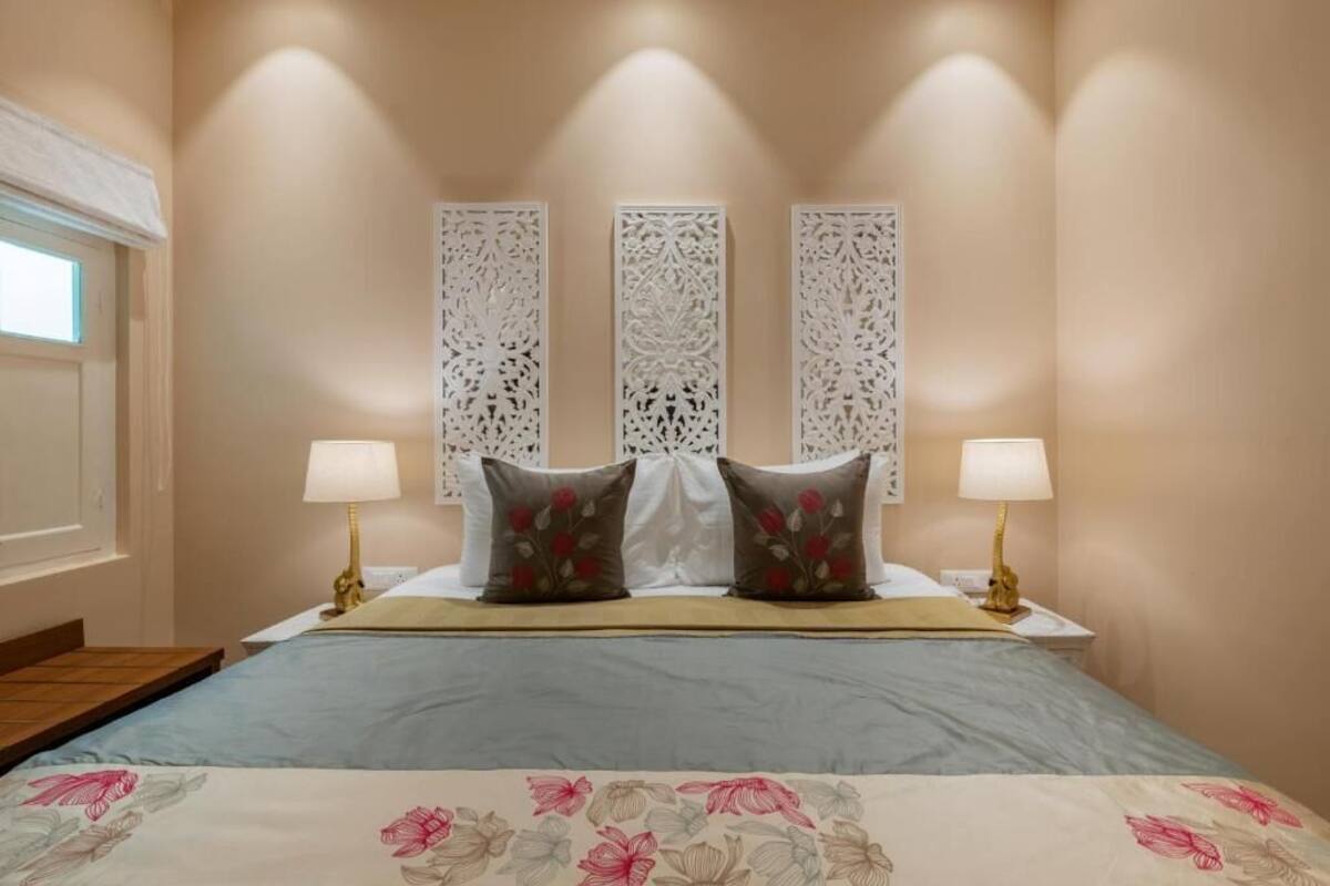A bedroom with a bed, two bedside lamps, decorative wall panels, and a window.