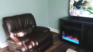 A brown leather sofa in a living room with a flat-screen TV on a wooden stand and a fireplace.